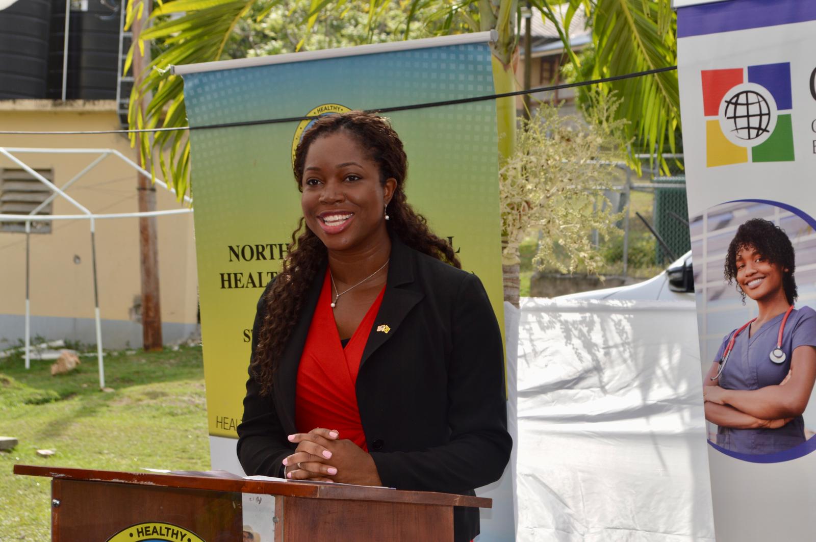 Oye speaking at a podium beside public-health displays.