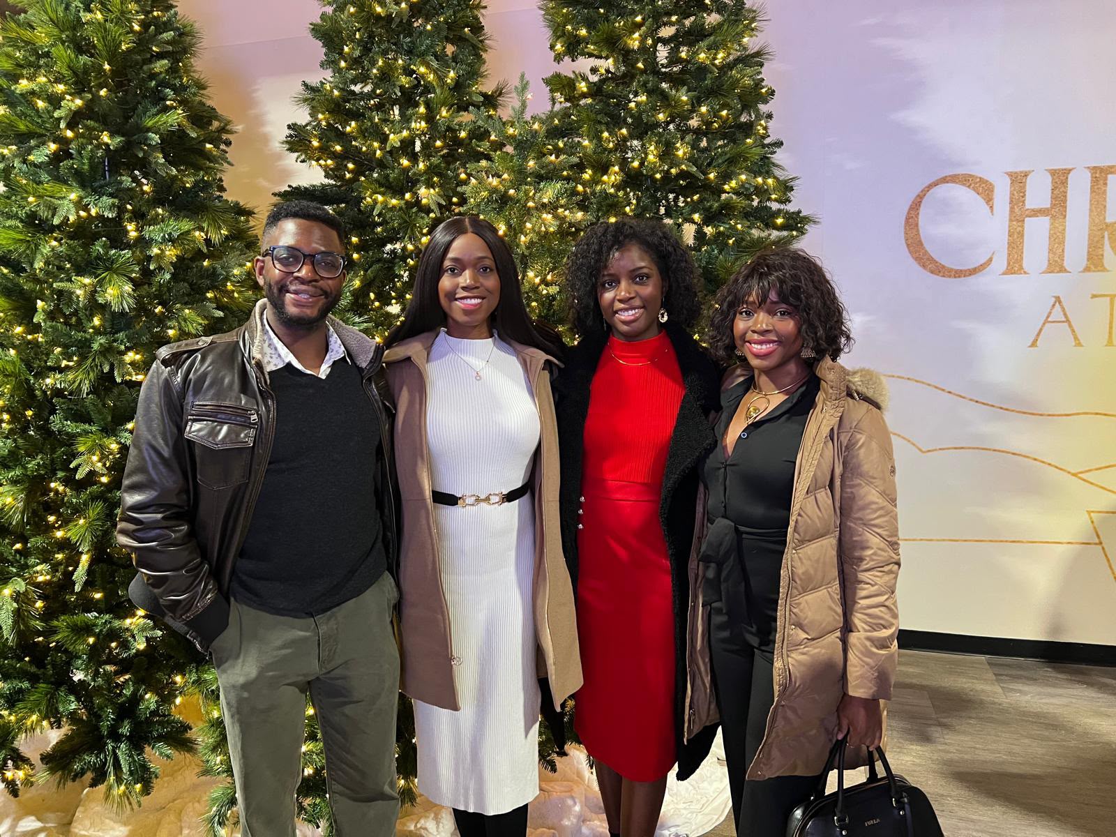 Four adults posing beside a decorated tree and seasonal display.