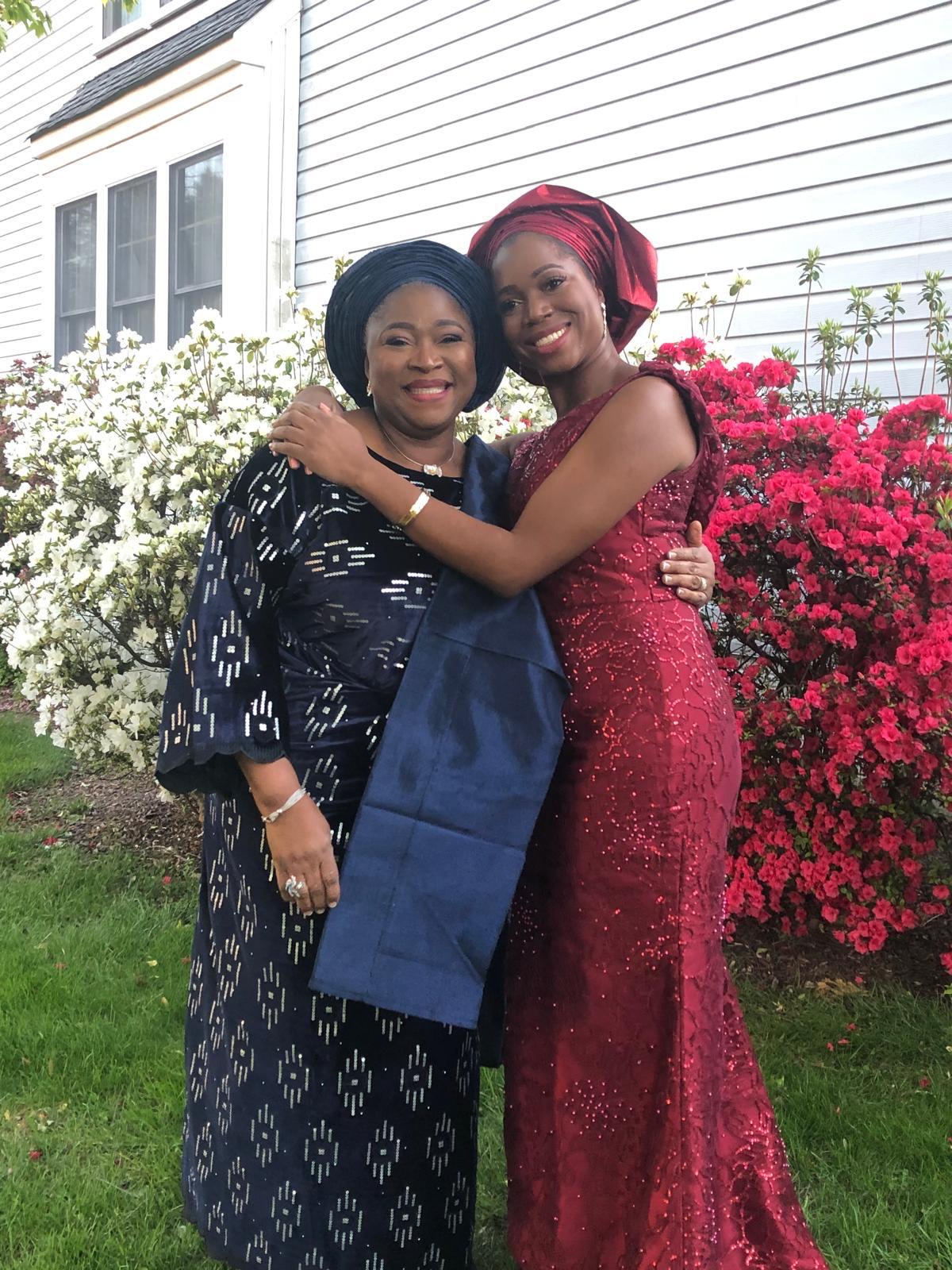 Two women embracing beside flowering shrubs.