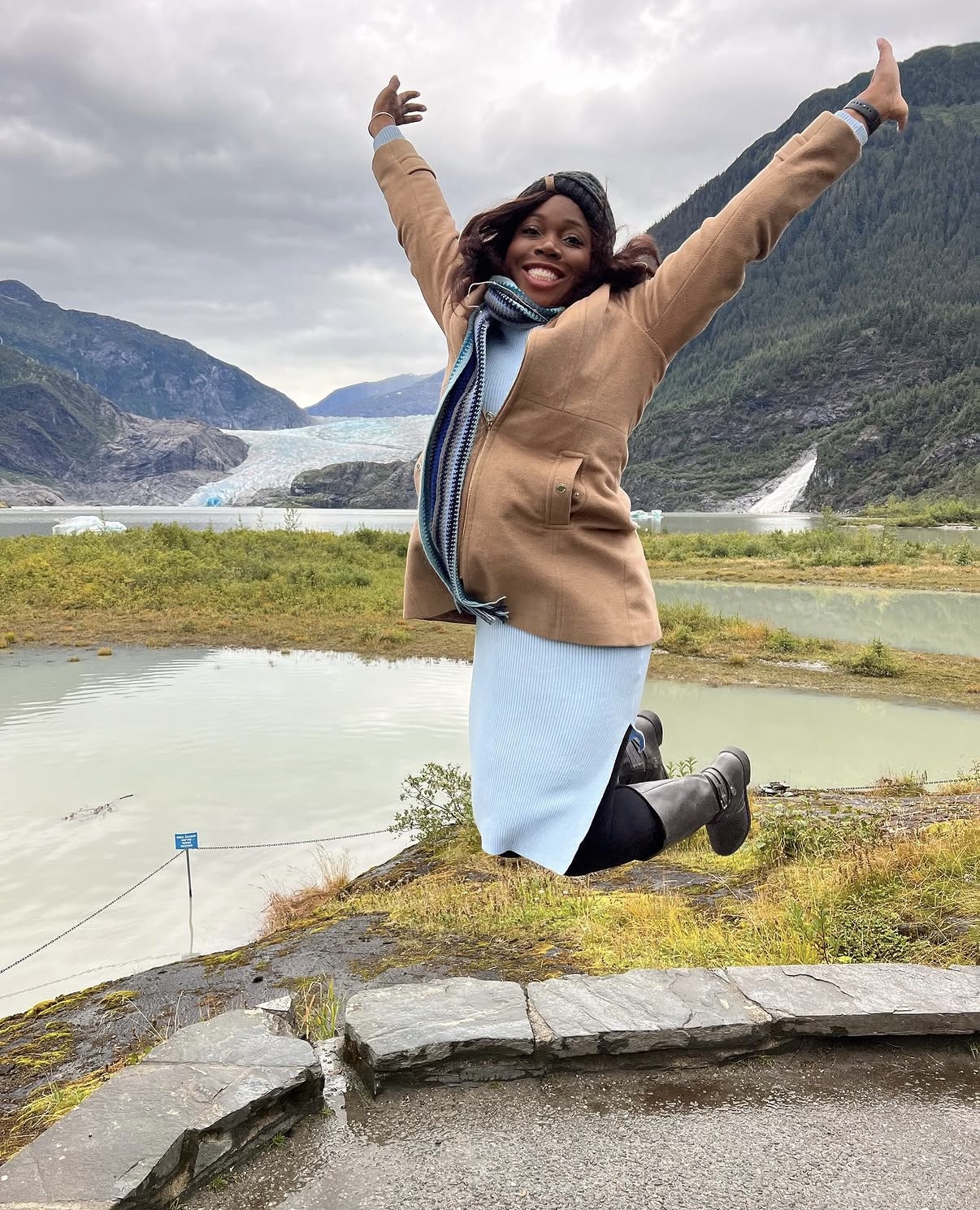 Oye leaping beside a mountain lake with her arms raised